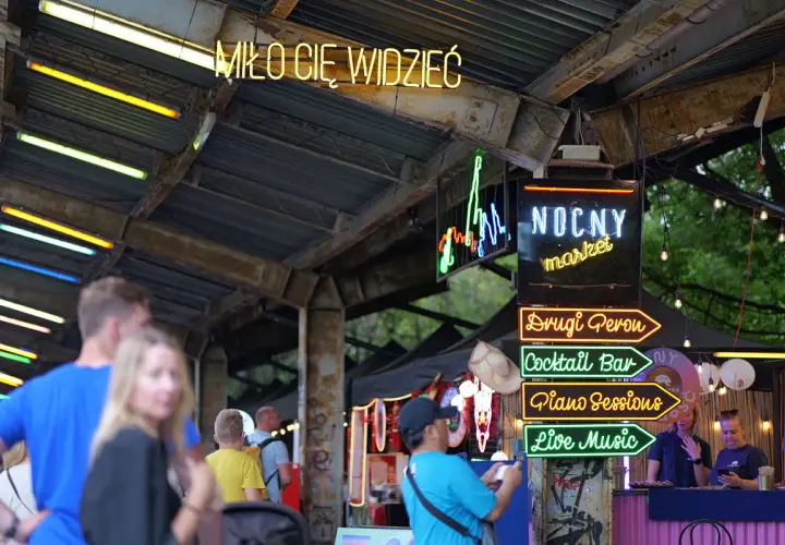Nocny market Warszawa wita neonami: "Miło Cię Widzieć", "Drugi Peron", "Cocktail Bar", "Piano Sessions", "Live Music".