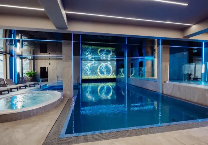 Nowoczesny basen i jacuzzi w rezydencji Aqua Szklarska Poręba. Niebieskie podświetlenie i ekran z animacją tworzą relaksującą atmosferę.