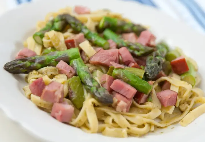 Pyszne spaghetti ze szparagami i kawałkami szynki na białym talerzu.