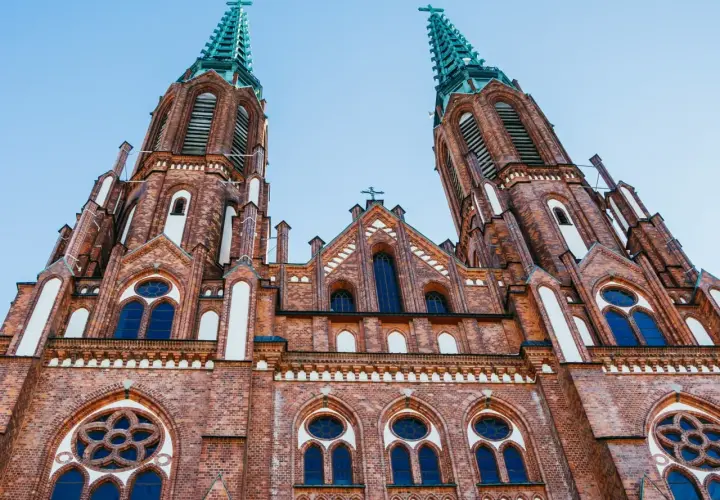 Dwie wieże ceglanego kościoła z zielonymi iglicami, jeden z najpiękniejszych kościołów w Polsce, pod błękitnym niebem.