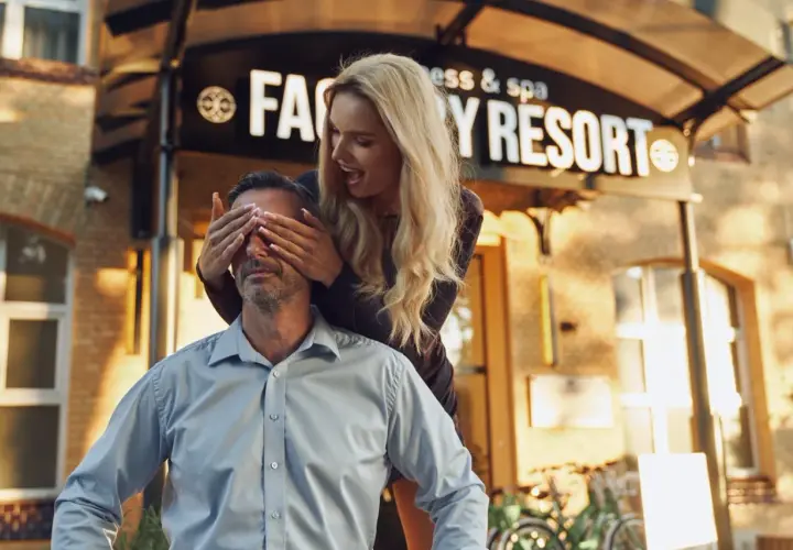 Zaskoczenie przed Factory Resort Kołobrzeg. Kobieta zakrywa oczy mężczyźnie, który uśmiecha się, czekając na niespodziankę.