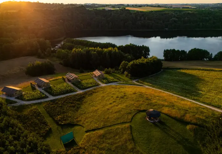Malownicze domki nad jeziorem, idealne na tani wypad na weekend w Polsce. Złote słońce oświetla zielone pola i lasy.
