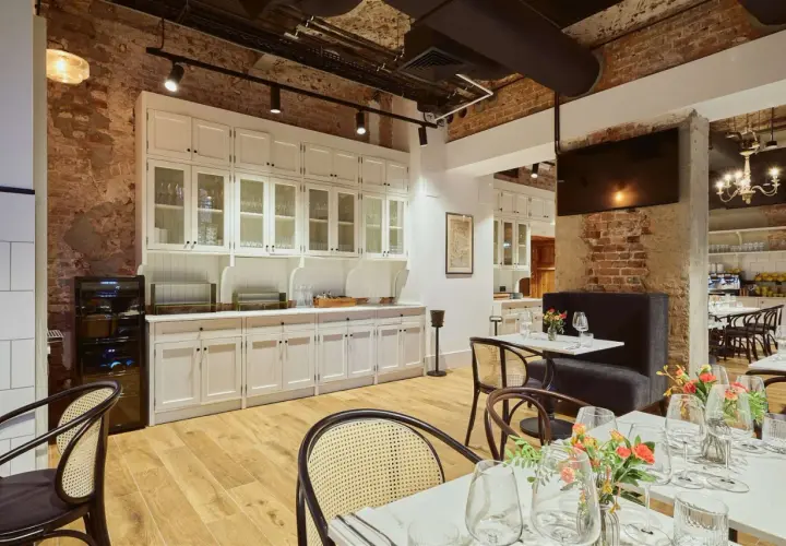 Eleganckie wnętrze restauracji Arche Klasztor Wrocław. Drewniana podłoga, ceglane ściany i białe meble tworzą przytulną atmosferę.