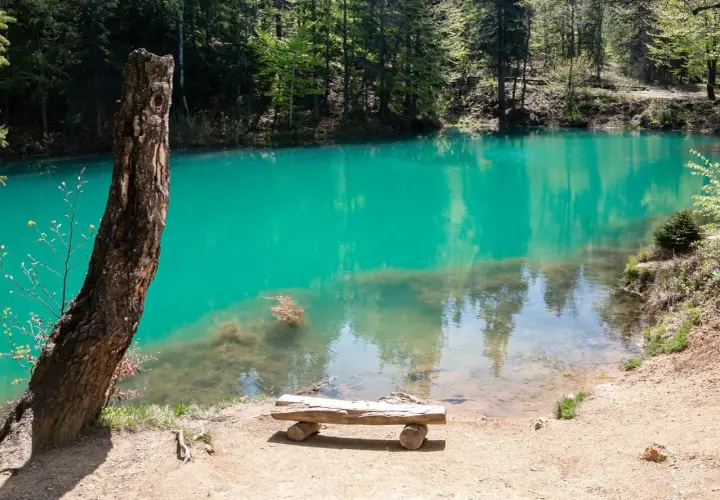 Turkusowe, **kolorowe jeziorka** otoczone lasem. Drewniana ławka zaprasza do odpoczynku nad wodą.