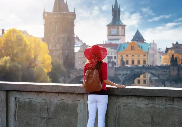Kobieta w czerwonym kapeluszu podziwia praskie praga nietypowe atrakcje, w tym Most Karola i wieże.