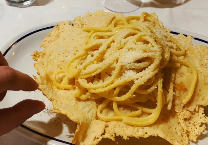Pyszne spaghetti z parmezanem, podane na chrupiącym serowym "gniazdku". Idealna odpowiedź na pytanie: co zjeść we Włoszech.