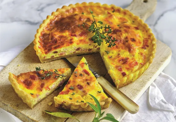 Pyszny quiche lorraine z boczkiem i ziołami, pokrojony na desce, z nożem i gałązkami tymianku.