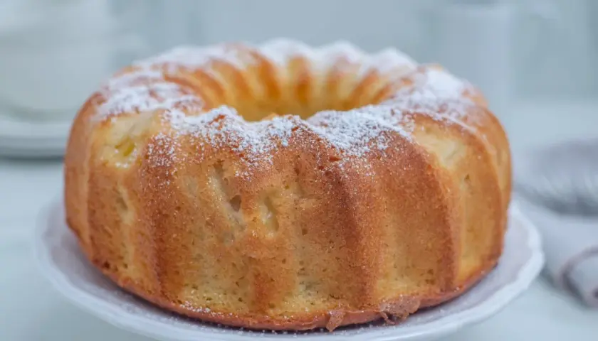 Puszysta babka wegańska, oprószona cukrem pudrem, prezentuje się apetycznie na białej paterze. Idealna na każdą okazję.