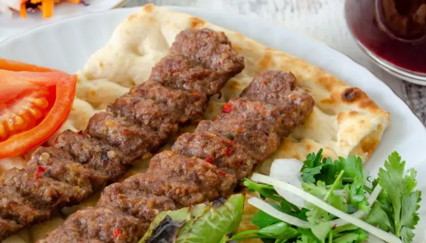 Pyszny Adana kebab przepis na talerzu z pitą, pomidorem, papryką i sałatką. Idealny na letni obiad.