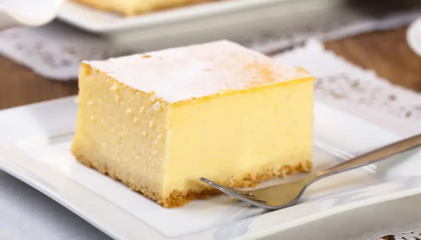 Pyszny kawałek new york cheesecake, oprószony cukrem pudrem, czeka na widelcu na talerzyku.