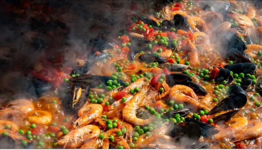 Pyszne hiszpańskie jedzenie: paella z krewetkami, małżami, groszkiem i pomidorami, parująca w wielkiej patelni.