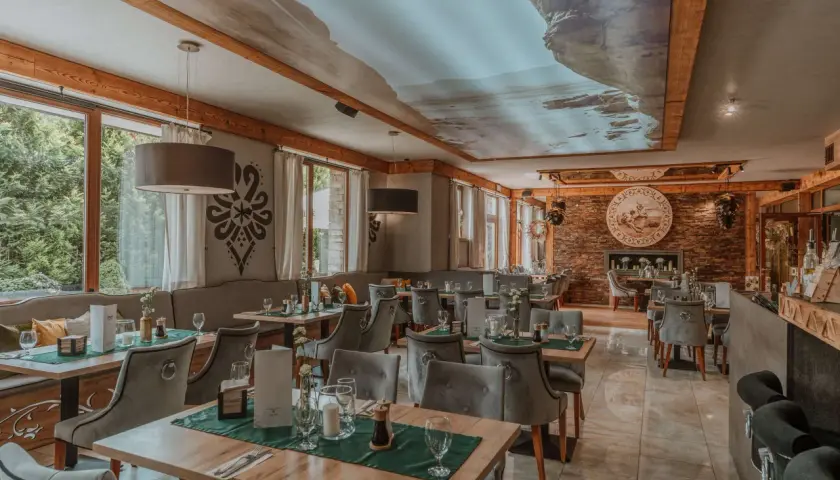 Przytulna restauracja w górach z widokiem na las. Drewniane belki, kamienne detale i sufit z malowniczym krajobrazem tworzą niepowtarzalny klimat.