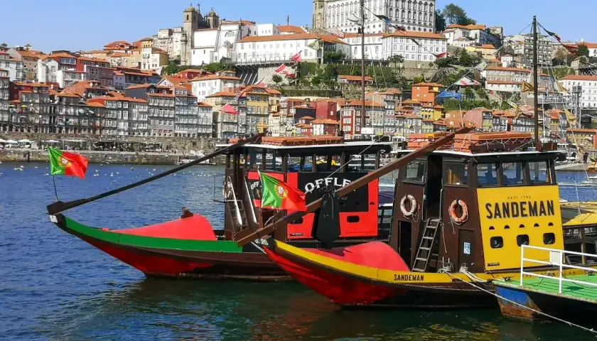Porto na weekend: tradycyjne łodzie Rabelo na rzece Douro, z kolorowymi domami i zabytkowymi budynkami w tle.
