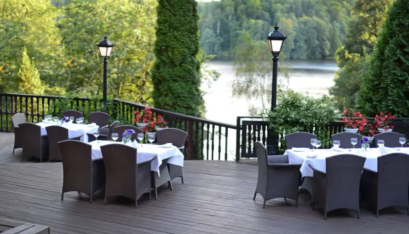 Elegancki taras z widokiem na jezioro, idealne miejsce na relaks w spa Mazury. Stoły nakryte do kolacji, otoczone zielenią.