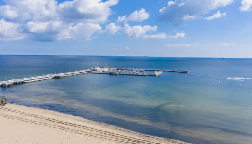 Molo z jachtami i żaglówkami, plaża i koparka – idealne atrakcje nad morzem dla każdego.