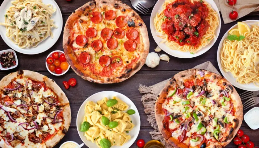 Uczta w stylu kuchnia włoska: pizze, spaghetti z klopsikami, fettuccine i tortellini na drewnianym stole.