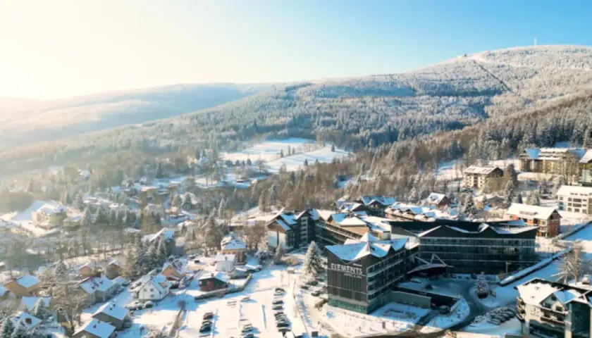 Malowniczy hotel ze stokiem w zimowej scenerii. Śnieg pokrywa dachy domów i drzewa, tworząc bajkowy krajobraz.