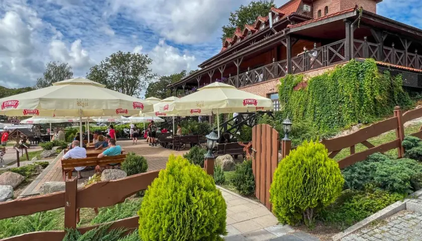 Letnie popołudnie w jednej z najlepszych restauracji na Mazurach. Goście odpoczywają pod parasolami, ciesząc się widokiem na jezioro.