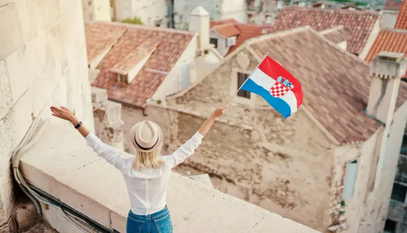 Kobieta z chorwacką flagą na tle dachów. Pozwala to na naukę podstawowych zwrotów po chorwacku.