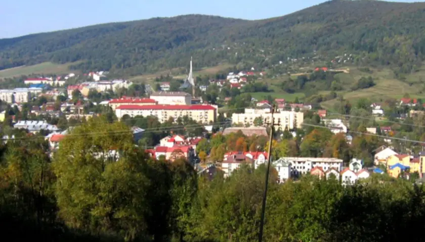 Widok na Ustrzyki Dolne z górami w tle. Miasto z czerwonymi dachami i nowoczesnymi budynkami, otoczone zielenią. Atrakcje turystyczne czekają!