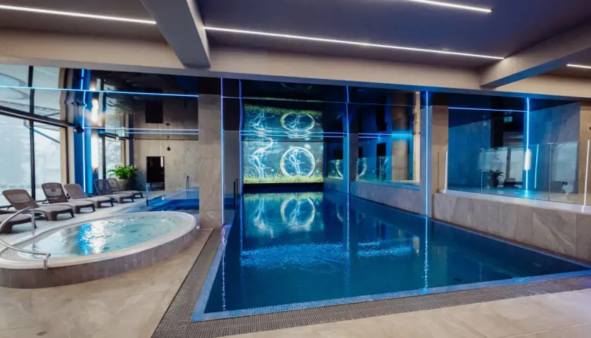 Nowoczesny basen i jacuzzi w rezydencji Aqua Szklarska Poręba. Niebieskie podświetlenie i ekran z animacją tworzą relaksującą atmosferę.