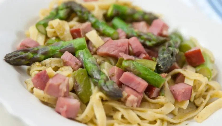 Pyszne spaghetti ze szparagami i kawałkami szynki na białym talerzu.