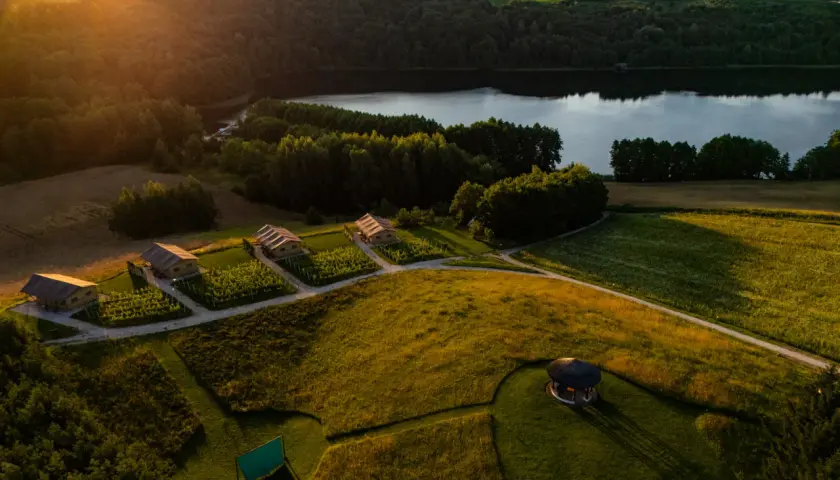 Malownicze domki nad jeziorem, idealne na tani wypad na weekend w Polsce. Złote słońce oświetla zielone pola i lasy.