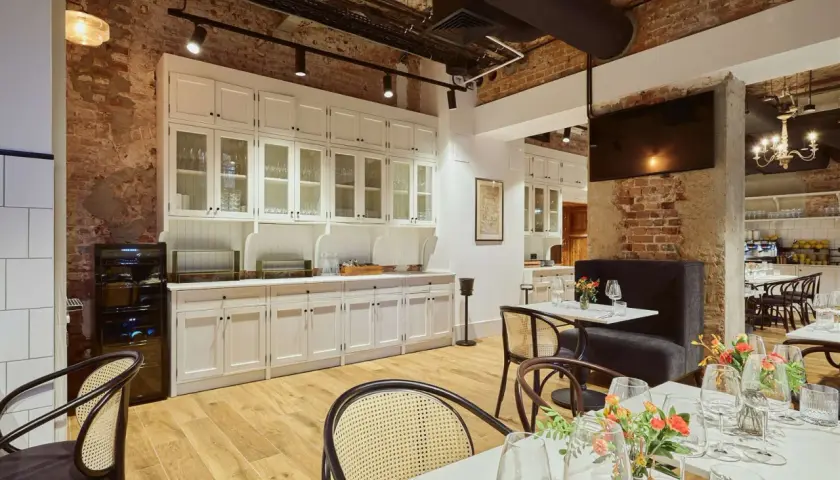 Eleganckie wnętrze restauracji Arche Klasztor Wrocław. Drewniana podłoga, ceglane ściany i białe meble tworzą przytulną atmosferę.