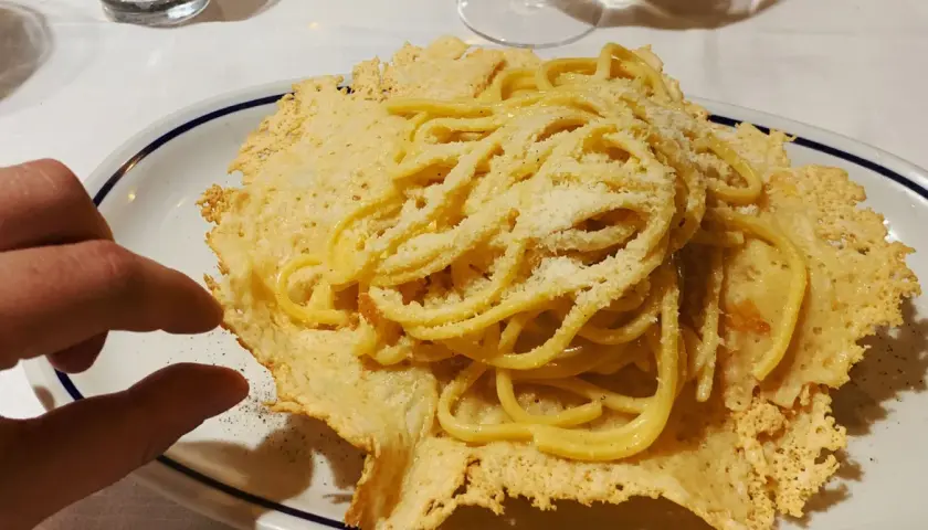 Pyszne spaghetti z parmezanem, podane na chrupiącym serowym "gniazdku". Idealna odpowiedź na pytanie: co zjeść we Włoszech.
