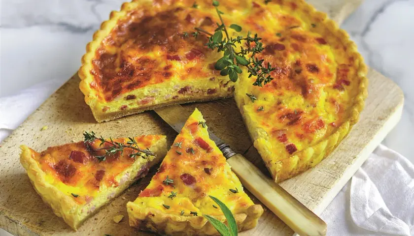Pyszny quiche lorraine z boczkiem i ziołami, pokrojony na desce, z nożem i gałązkami tymianku.