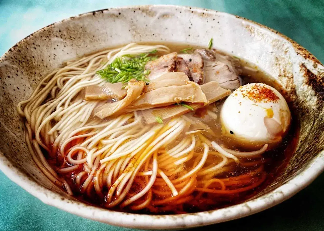 Pyszny, domowy ramen z makaronem, plastrami mięsa, bambusem i jajkiem na twardo, posypany szczypiorkiem i papryką.