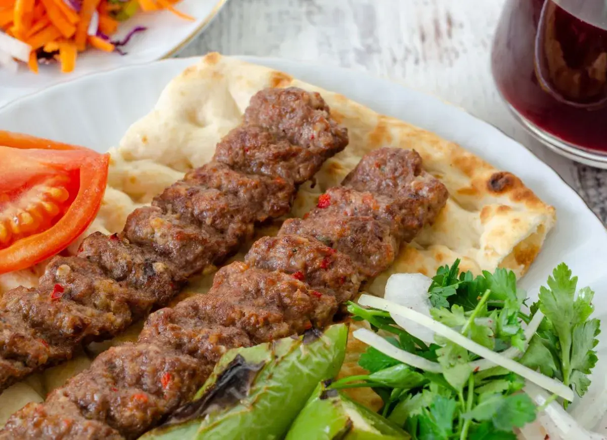 Pyszny Adana kebab przepis na talerzu z pitą, pomidorem, papryką i sałatką. Idealny na letni obiad.