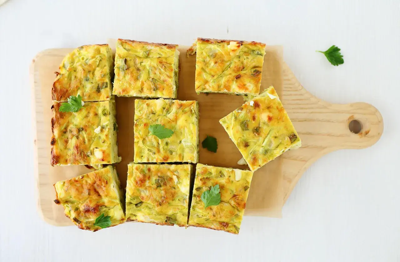 Pyszna frittata z cukinią pokrojona w kwadraty, ułożona na desce.