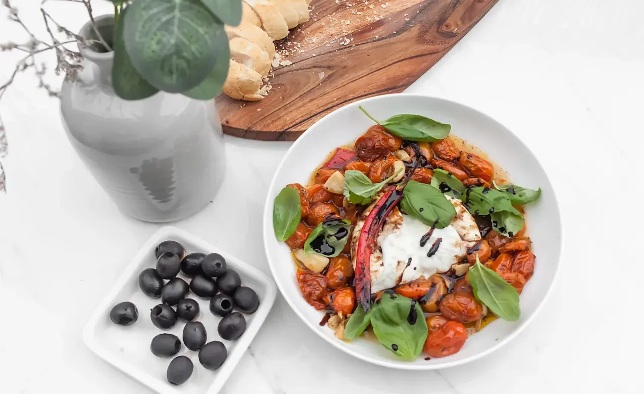 Pyszny burrata przepis: kremowy ser z pieczonymi pomidorkami, czosnkiem, bazylią i oliwkami. Idealny na letni obiad.