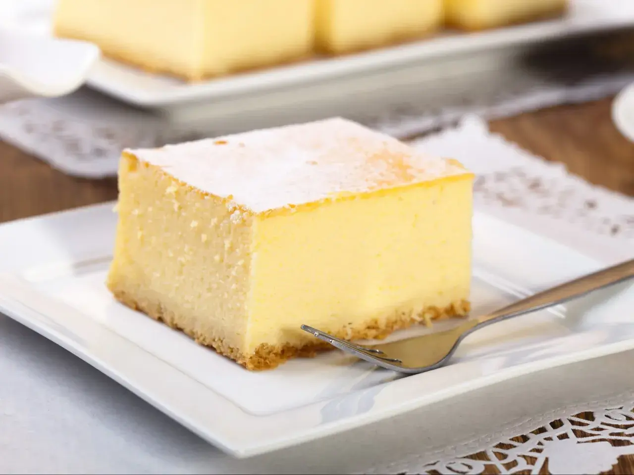 Pyszny kawałek new york cheesecake, oprószony cukrem pudrem, czeka na widelcu na talerzyku.