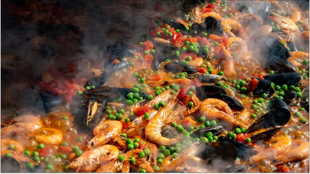 Pyszne hiszpańskie jedzenie: paella z krewetkami, małżami, groszkiem i pomidorami, parująca w wielkiej patelni.