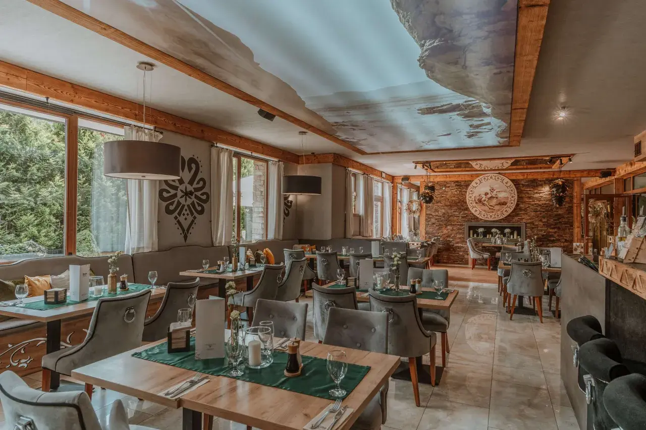 Przytulna restauracja w górach z widokiem na las. Drewniane belki, kamienne detale i sufit z malowniczym krajobrazem tworzą niepowtarzalny klimat.