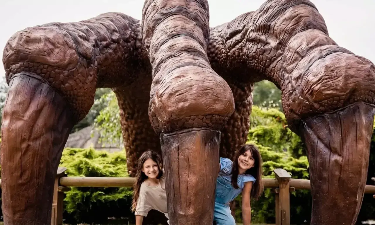 Dwie dziewczynki ukrywają się za gigantycznymi łapami dinozaura. Wspaniałe lublin atrakcje dla dzieci!