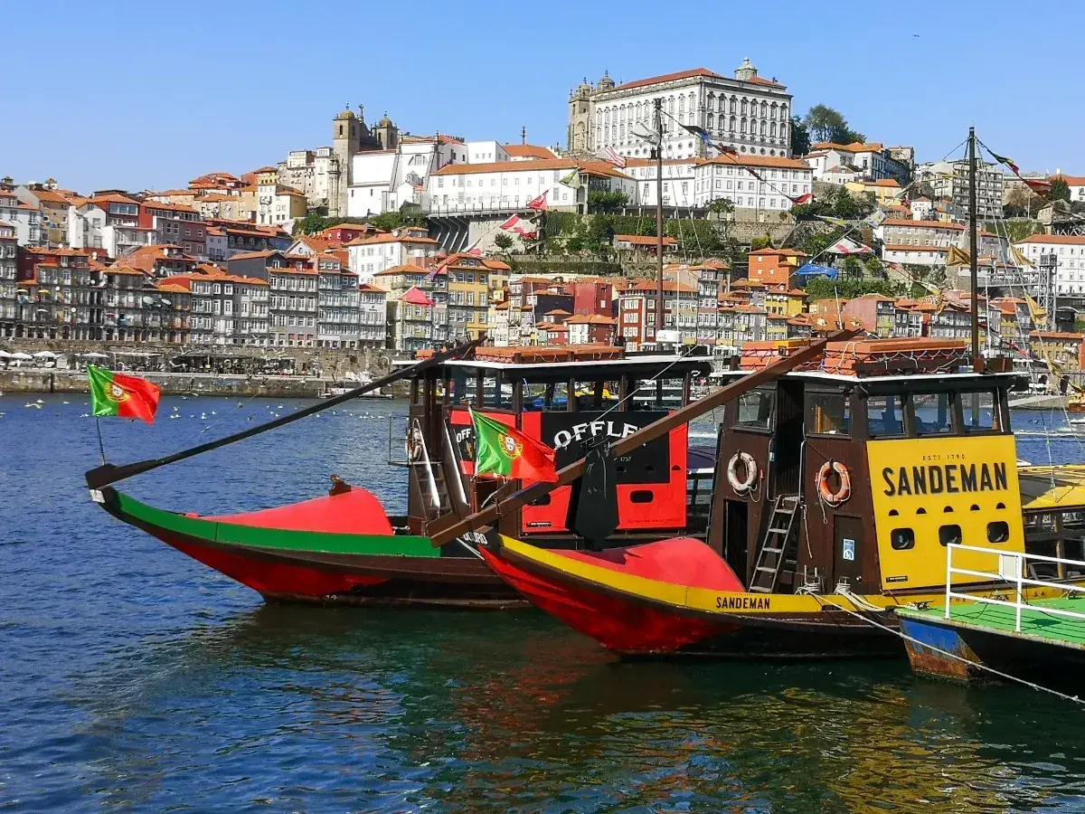 Porto na weekend: tradycyjne łodzie Rabelo na rzece Douro, z kolorowymi domami i zabytkowymi budynkami w tle.
