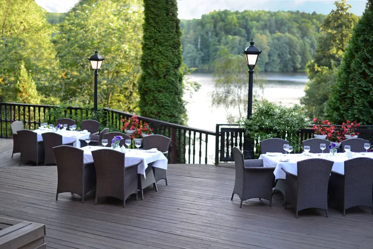 Elegancki taras z widokiem na jezioro, idealne miejsce na relaks w spa Mazury. Stoły nakryte do kolacji, otoczone zielenią.