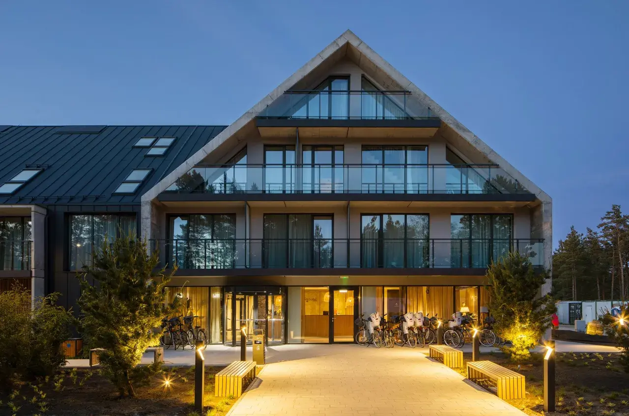 Nowoczesny budynek Saltic Resort & Spa Łeba z betonowymi elementami i przeszklonymi balkonami, oświetlony wieczorem.