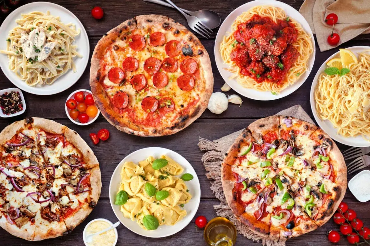 Uczta w stylu kuchnia włoska: pizze, spaghetti z klopsikami, fettuccine i tortellini na drewnianym stole.