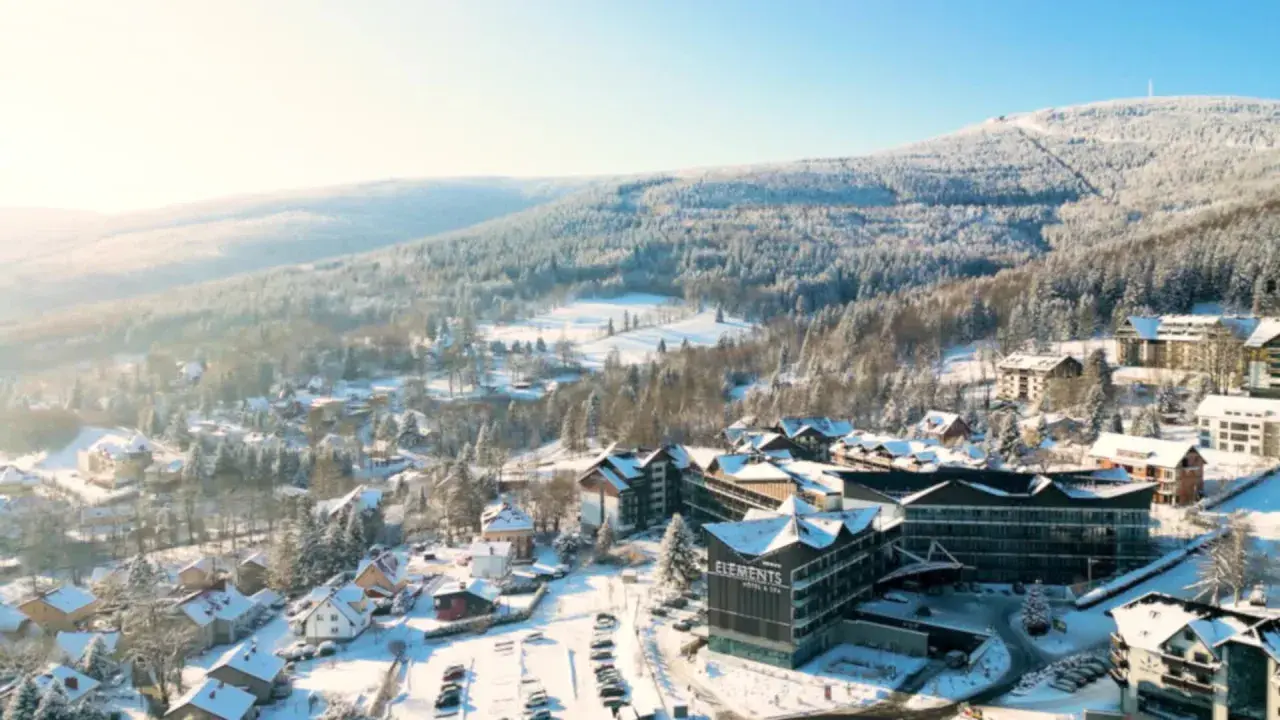 Malowniczy hotel ze stokiem w zimowej scenerii. Śnieg pokrywa dachy domów i drzewa, tworząc bajkowy krajobraz.