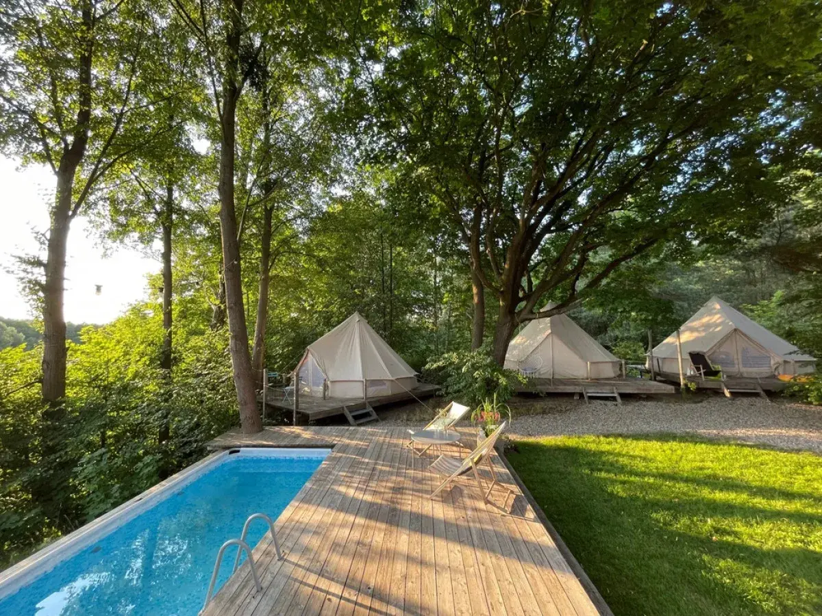 Luksusowy glamping nad jeziorem: namioty tipi na drewnianych tarasach, basen i leżaki wśród drzew. Idealne miejsce na relaks.