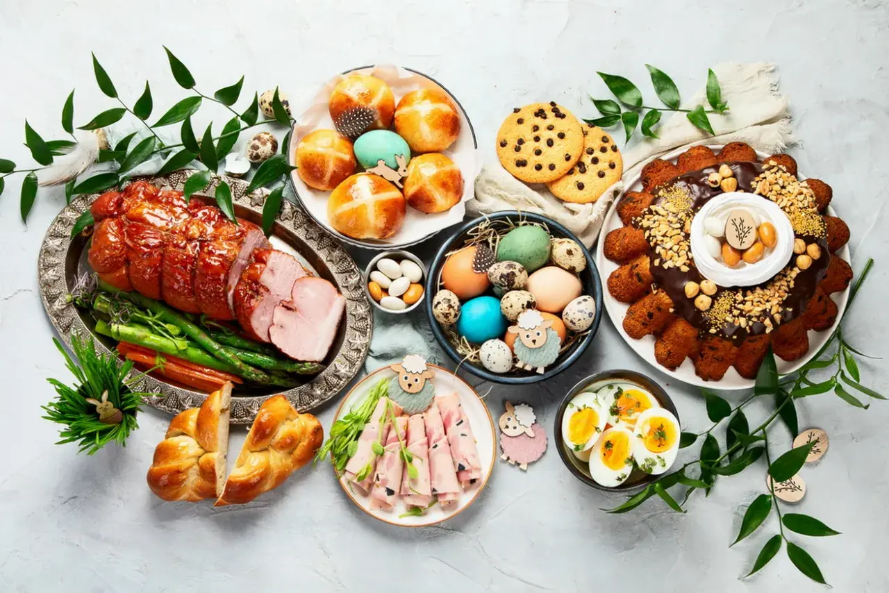 Wielkanocny stół z pieczonym mięsem, babkami, jajkami, ciastkami i dekoracjami.