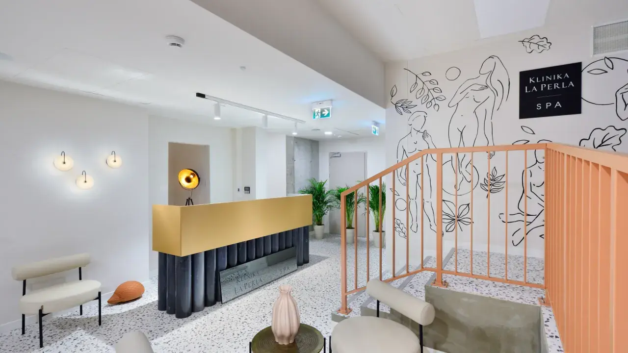 Nowoczesne wnętrze kliniki La Perla SPA w Nałęczowie. Złota recepcja, schody z brzoskwiniową balustradą i artystyczne rysunki na ścianie tworzą elegancką atmosferę.