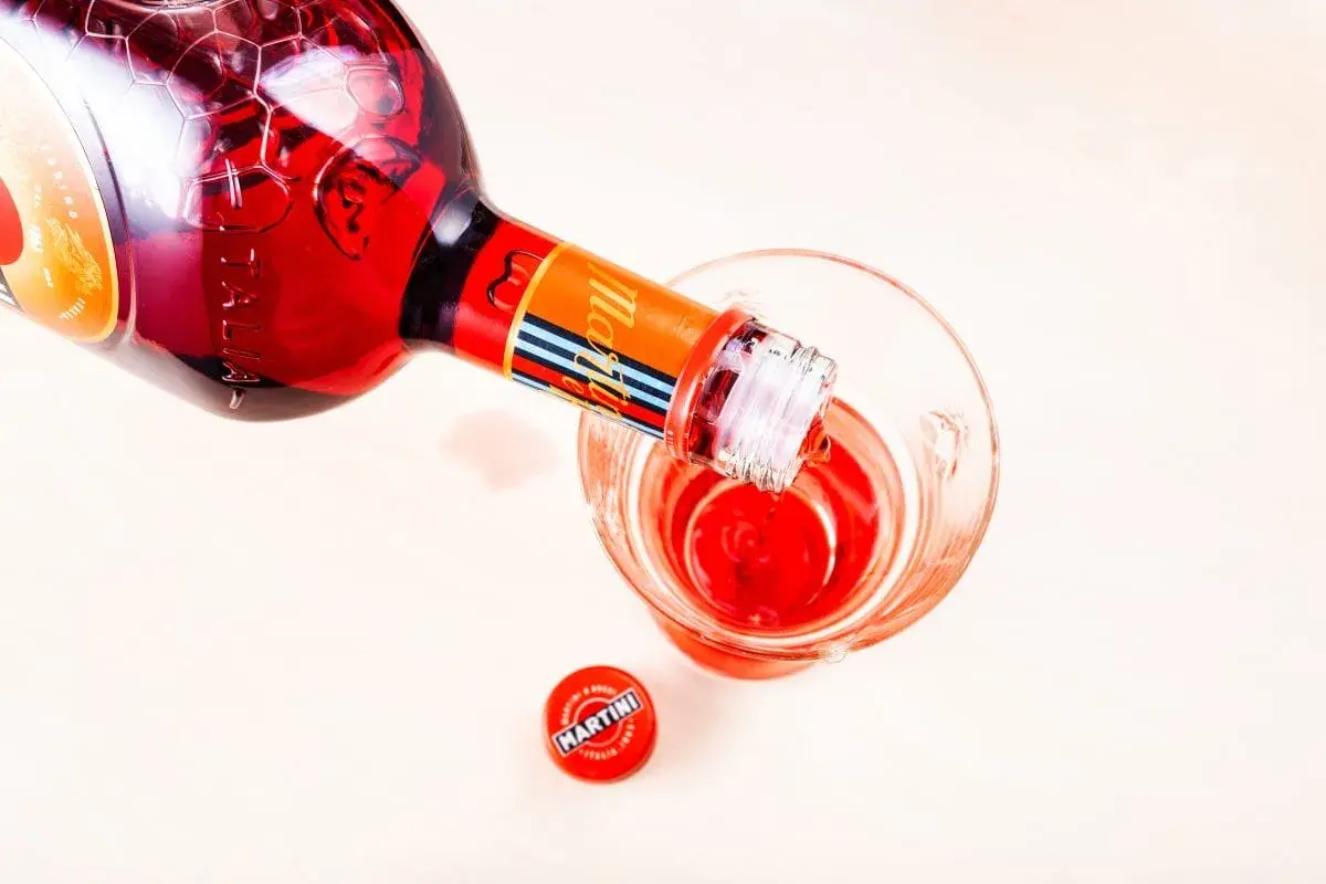 Czerwony Martini Fiero Tonic nalewany do szklanki. Obok leży czerwona zakrętka z logo Martini.