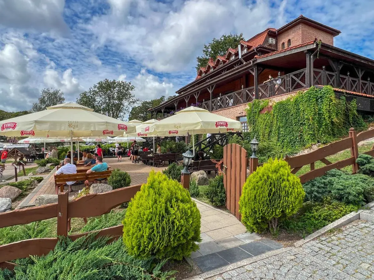 Letnie popołudnie w jednej z najlepszych restauracji na Mazurach. Goście odpoczywają pod parasolami, ciesząc się widokiem na jezioro.