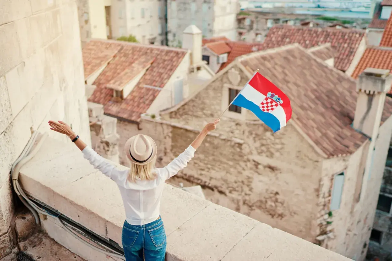 Kobieta z chorwacką flagą na tle dachów. Pozwala to na naukę podstawowych zwrotów po chorwacku.