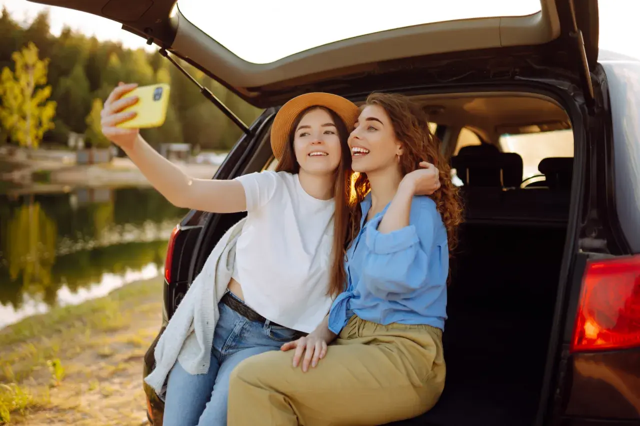 Dwie przyjaciółki robią sobie selfie nad jeziorem, ciesząc się wspólnym weekendem.